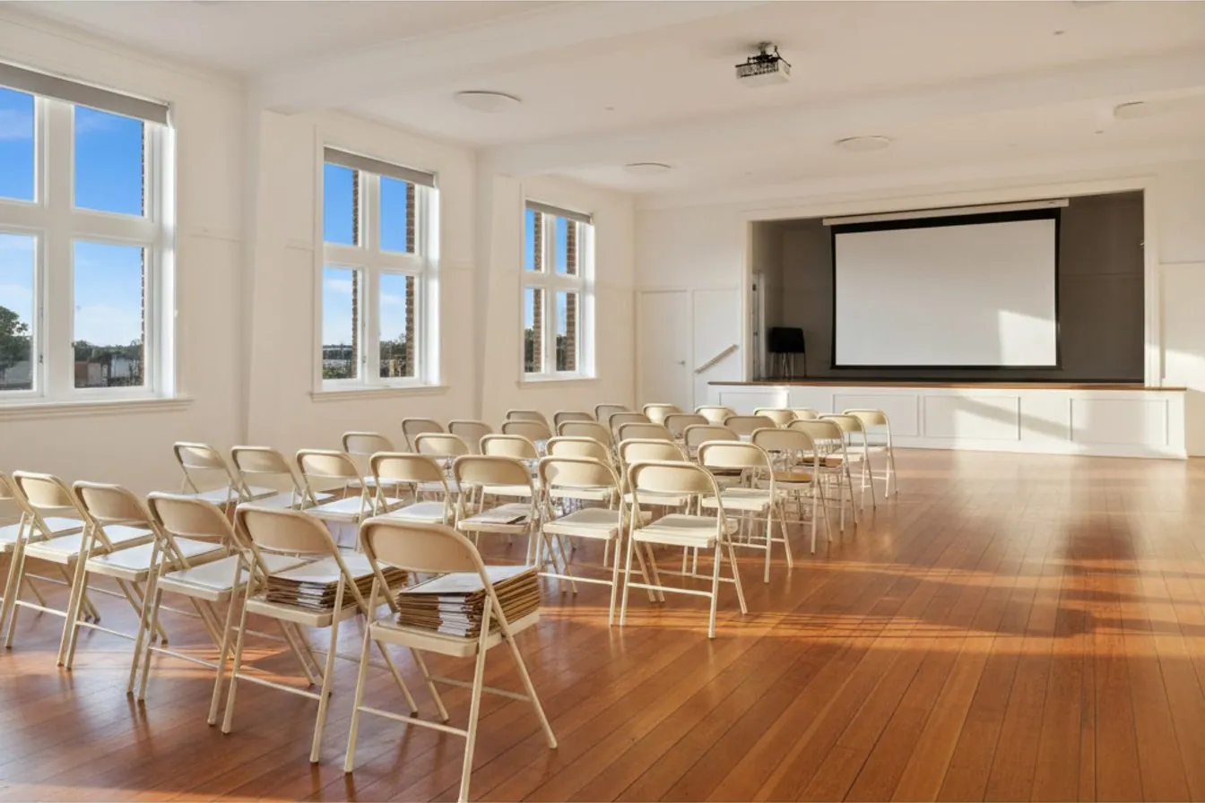 An empty half of a community hall with chairs still unfilled, suggesting a grant pool draining before its listed closing date.
