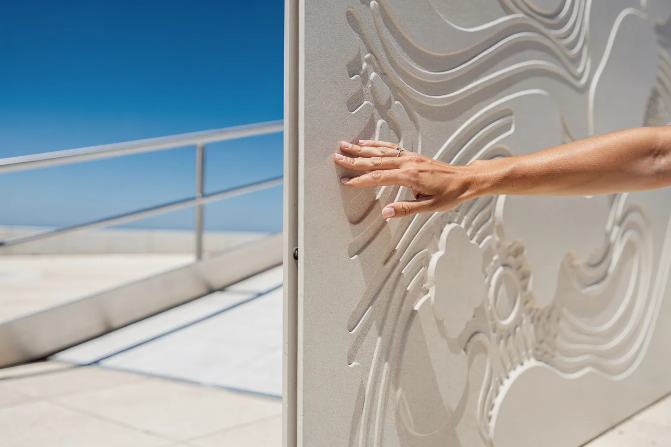 A hand reads a tactile braille panel beside an accessible ramp, a detail of careful planning.